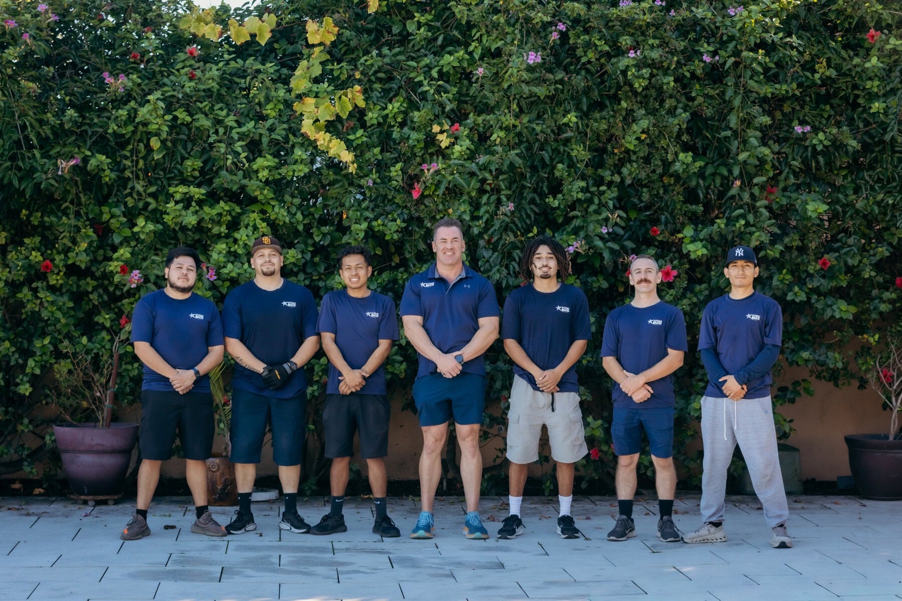 Unified team of 1st Choice Movers standing against a green hedge backdrop.
